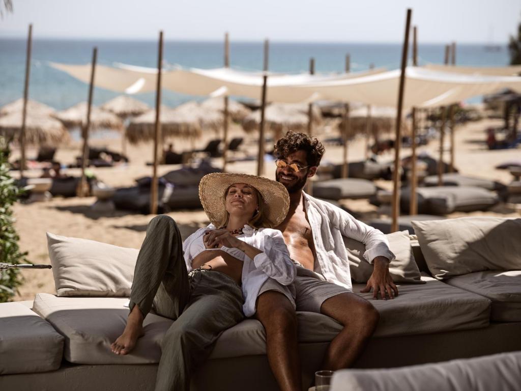 a man and woman sitting on a couch at the beach at The Bay Hotel & Suites in Vasilikos