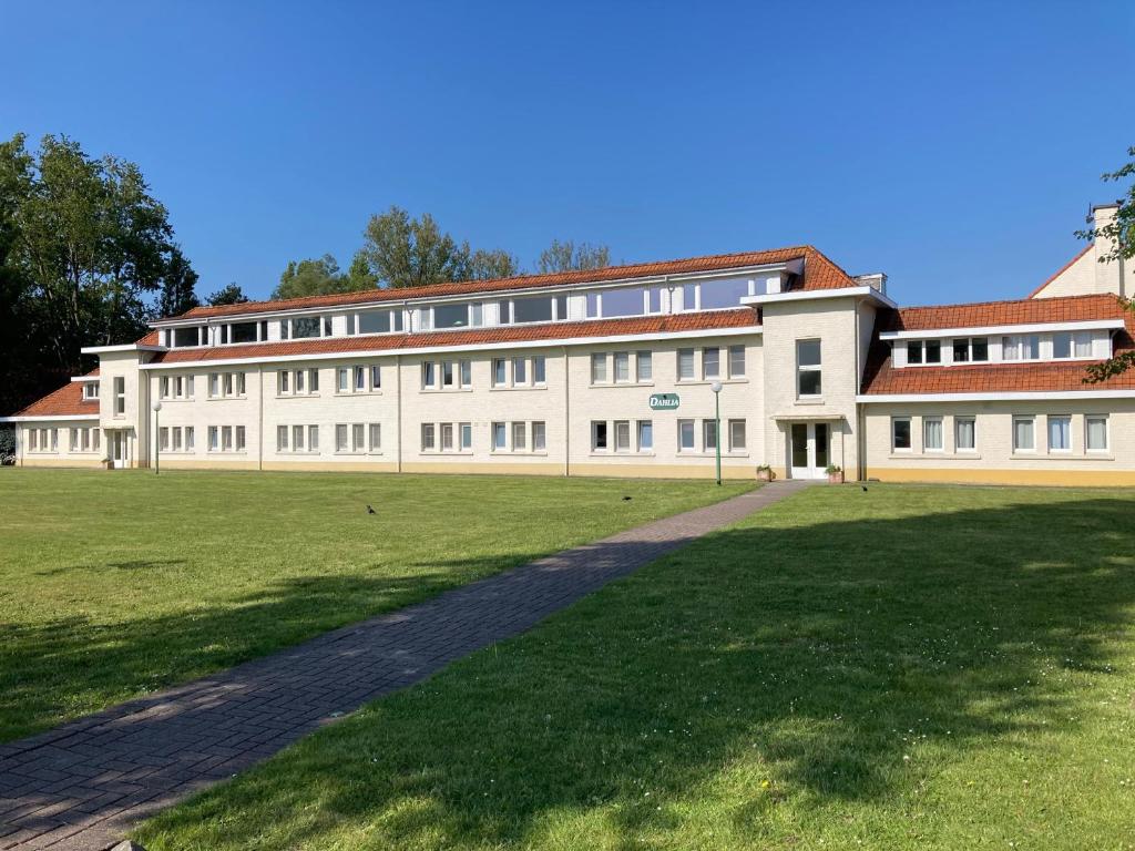 ein großes weißes Gebäude mit einem Grasfeld davor in der Unterkunft Dahlia 107 - zonnig en volledig uitgerust appartement in De Haan