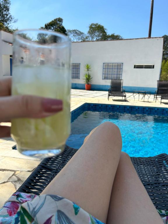 a woman holding a glass of beer next to a pool at Chalézinho Santorini in Guararema