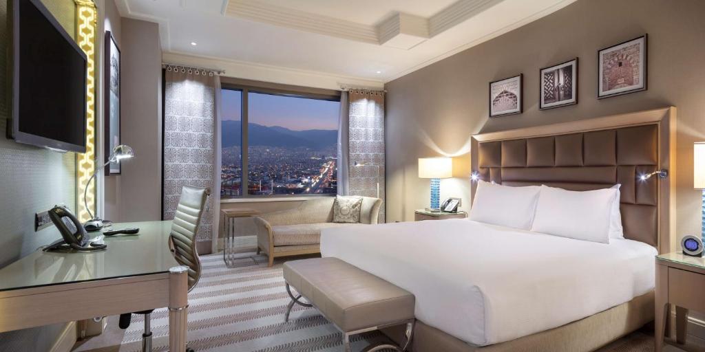 Schlafzimmer mit einem großen weißen Bett, einem Schreibtisch und einem Fenster in der Unterkunft Hilton Bursa Convention Center & Spa in Bursa