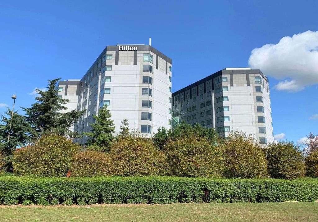 two high rise buildings with trees in front of a park at Hilton Paris Charles De Gaulle Airport in Roissy-en-France
