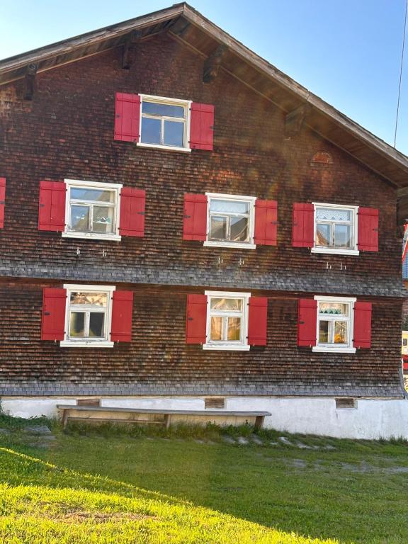a building with red shuttered windows and a bench in front at Great old WÄLDERHAUS in Au im Bregenzerwald