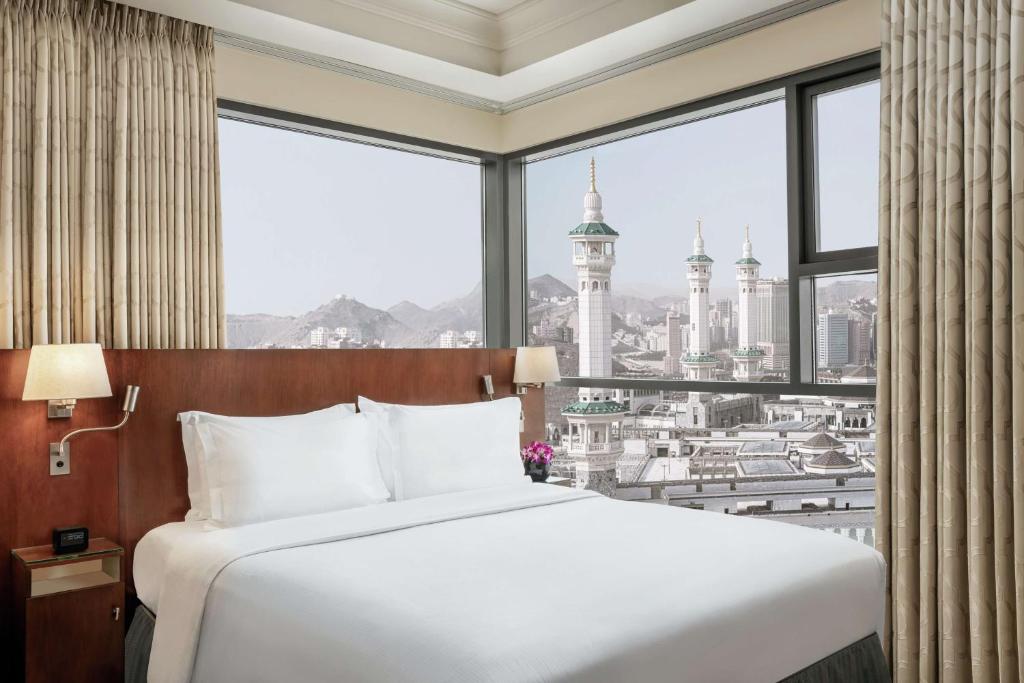a bed in a room with a large window at Hilton Suites Jabal Omar Makkah in Mecca