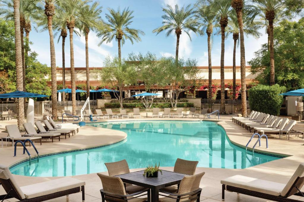 a pool with chairs and tables and palm trees at Hilton Scottsdale Resort & Villas in Scottsdale