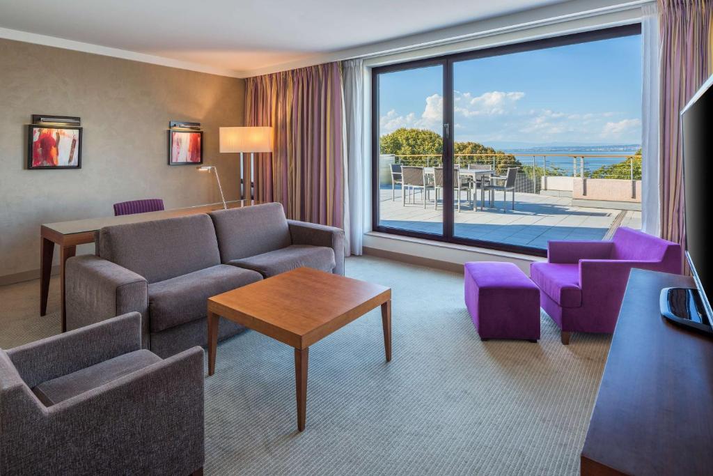 a living room with a couch and chairs and a large window at Hilton Evian Les Bains in Évian-les-Bains