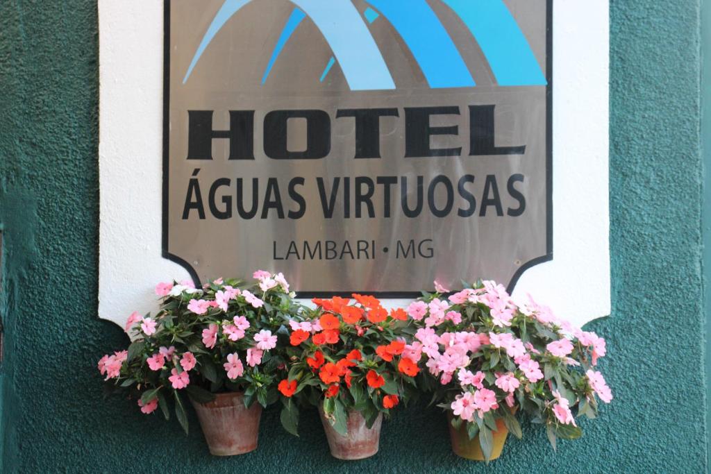 un cartel de hotel con tres macetas de flores en una pared en Hotel Águas Virtuosas, en Lambari
