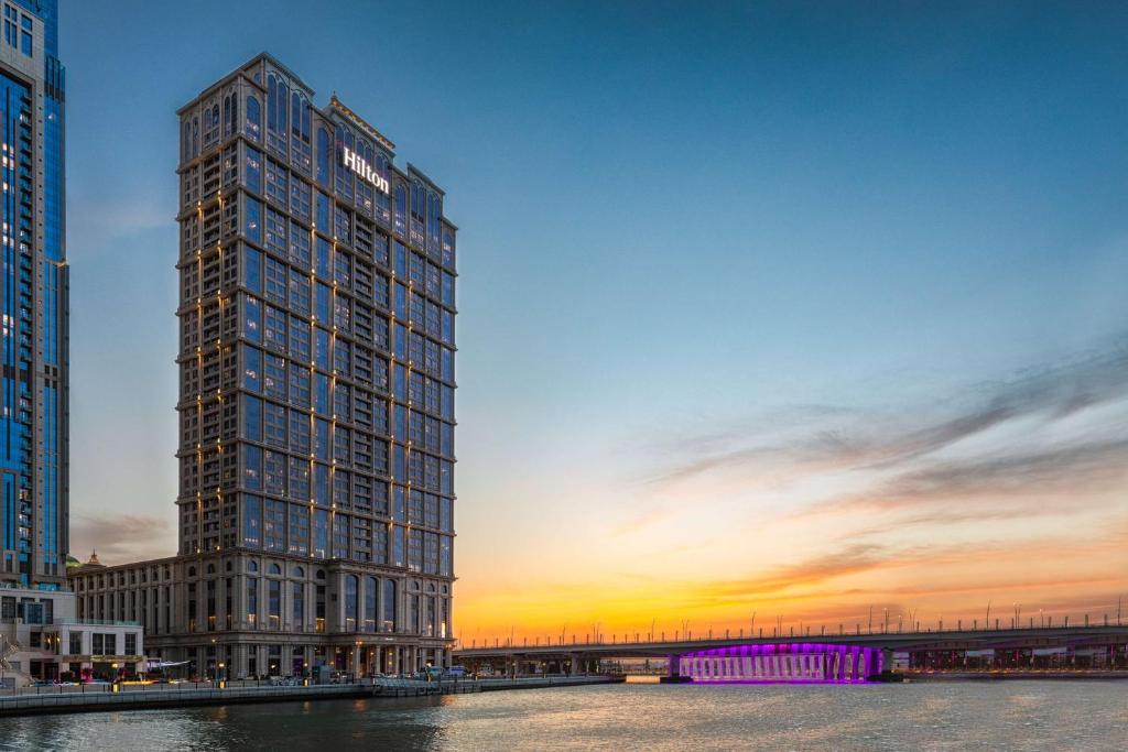 un grand bâtiment avec un coucher de soleil en arrière-plan dans l'établissement Hilton Dubai Al Habtoor City, à Dubaï