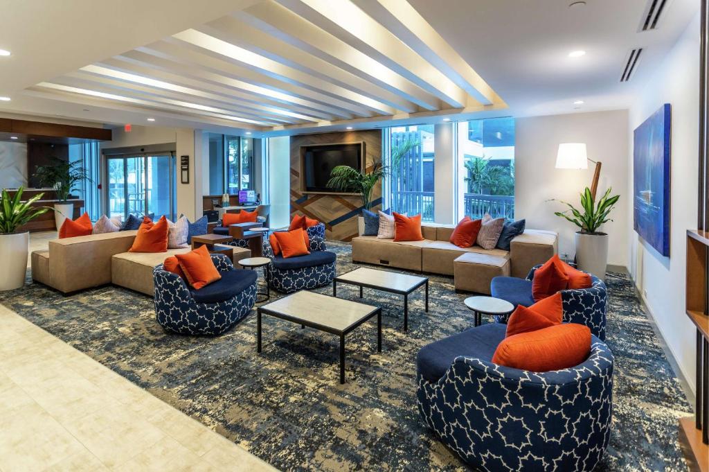 Una sala de estar con sofás, mesas y ventanas. en Hilton Garden Inn West Palm Beach I95 Outlets, en West Palm Beach