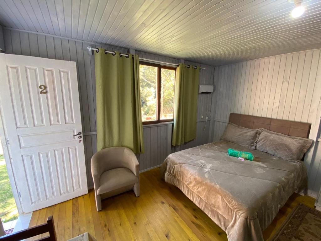 um quarto com uma cama, uma cadeira e uma janela em Cabana Pé Da Serra dos Bitus em Urubici