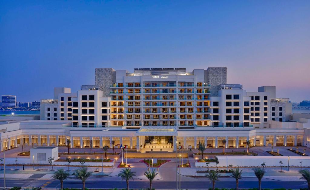 a large white building with palm trees in front of it at Hilton Abu Dhabi Yas Island in Abu Dhabi