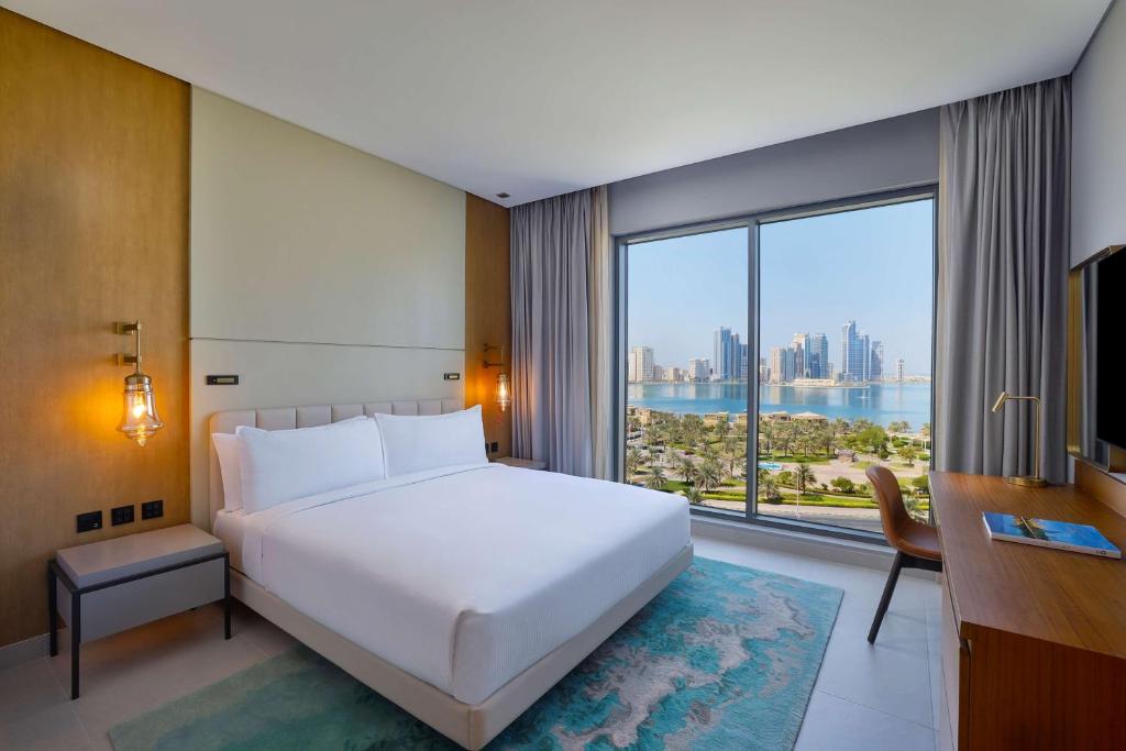 DoubleTree by Hilton Sharjah Waterfront Hotel And Residences في الشارقة: غرفة نوم بسرير ابيض كبير ونافذة كبيرة