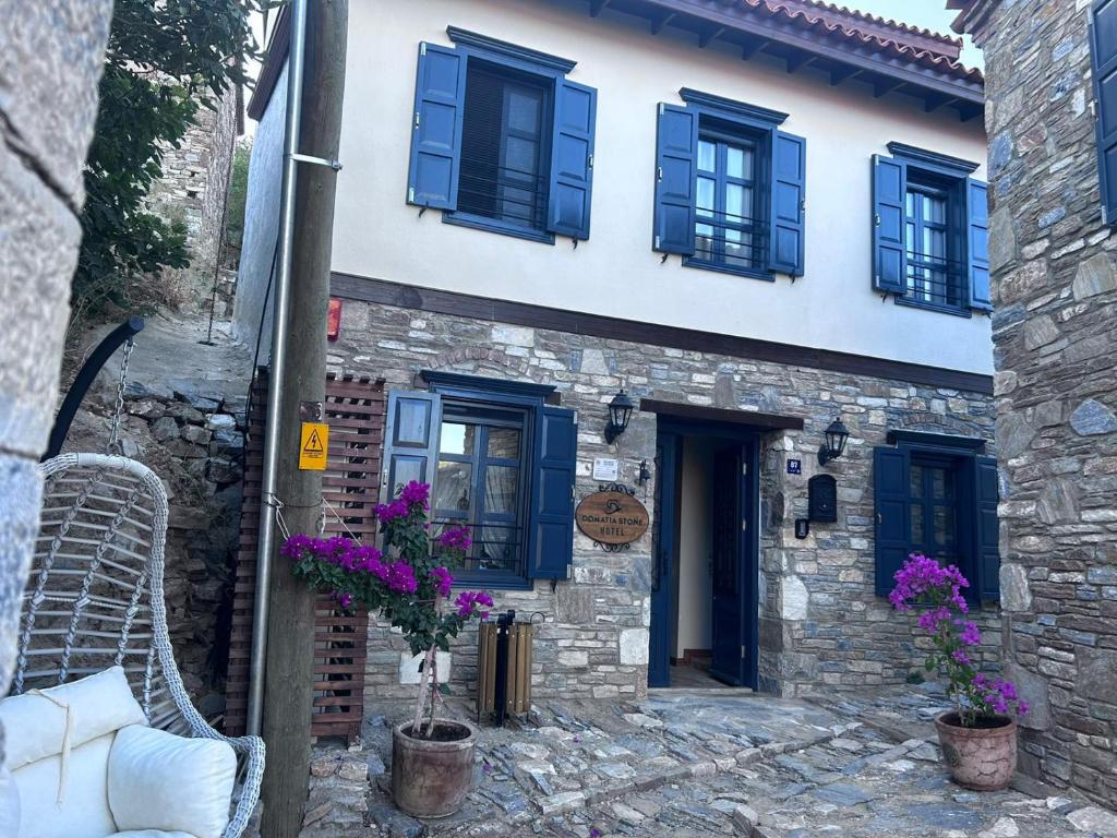 Casa de piedra con ventanas azules y flores púrpuras en Domatia Stone Hotel, en Soke