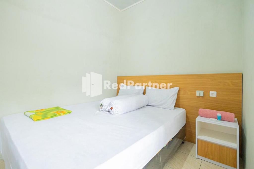 - une chambre avec un lit blanc et une tête de lit en bois dans l'établissement Atiq Homestay Syariah Mitra RedDoorz, à Serang