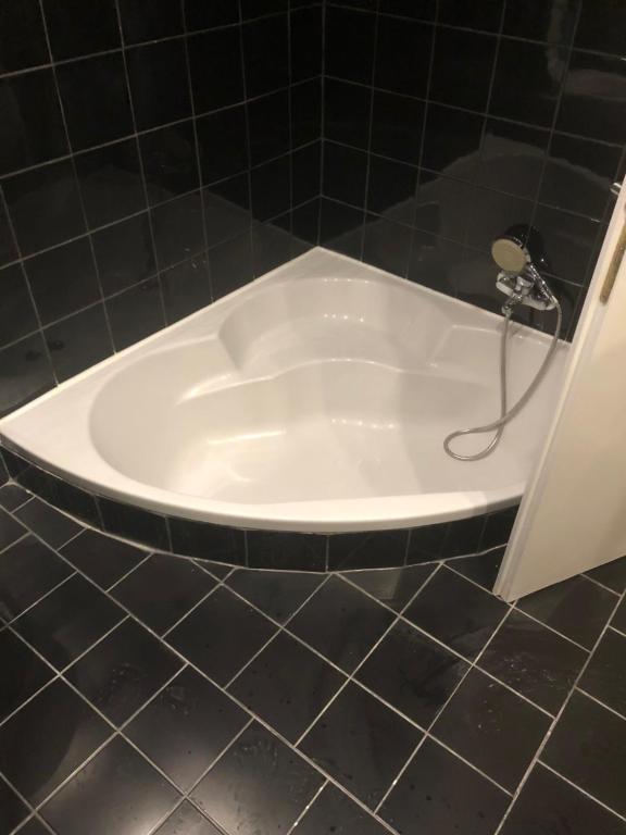 a white bath tub in a black tiled bathroom at Deep City Vienna in Vienna