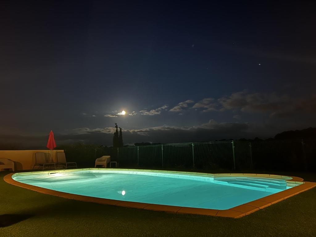 a swimming pool at night with the moon in the sky at Hôtel Restaurant La Bergerie in Aragon