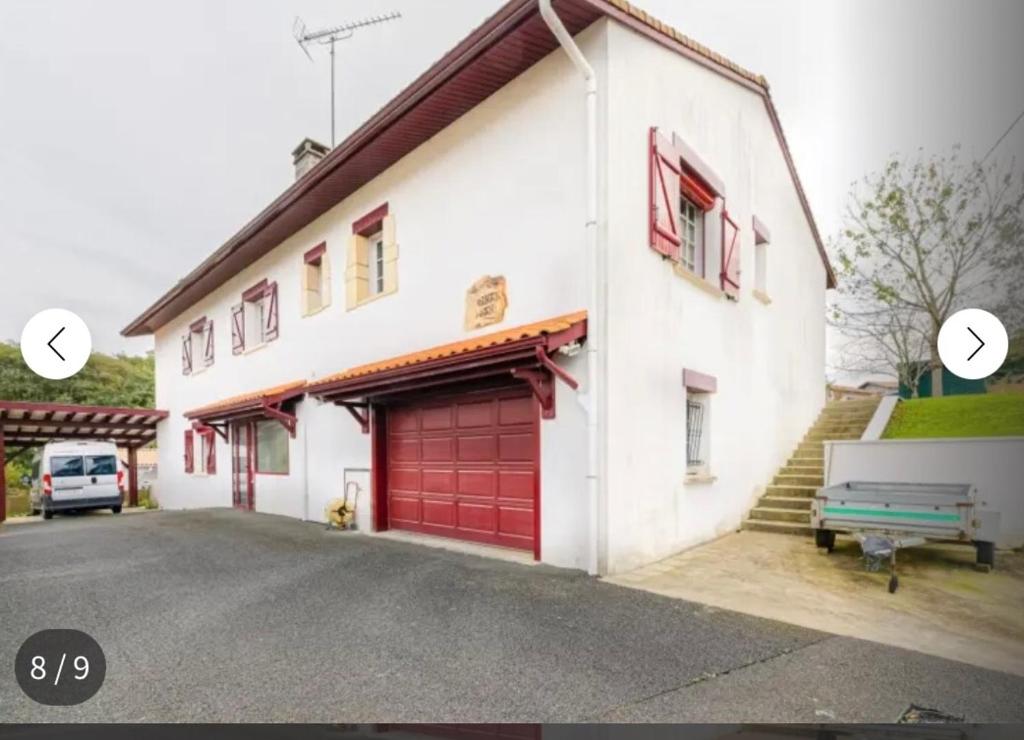 a white building with red garage doors and a bench at Joli Appartement Proche Plage in Ahetze