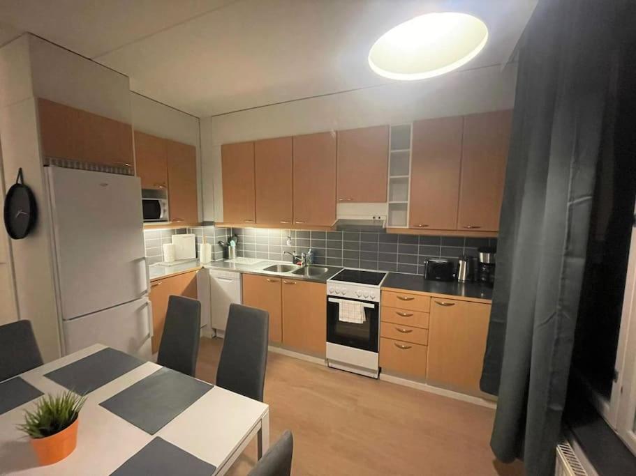 eine Küche mit braunen Schränken, einem Tisch und einem weißen Kühlschrank in der Unterkunft Kotimaailma - Saunallinen kolmio Herttoniemessä in Helsinki