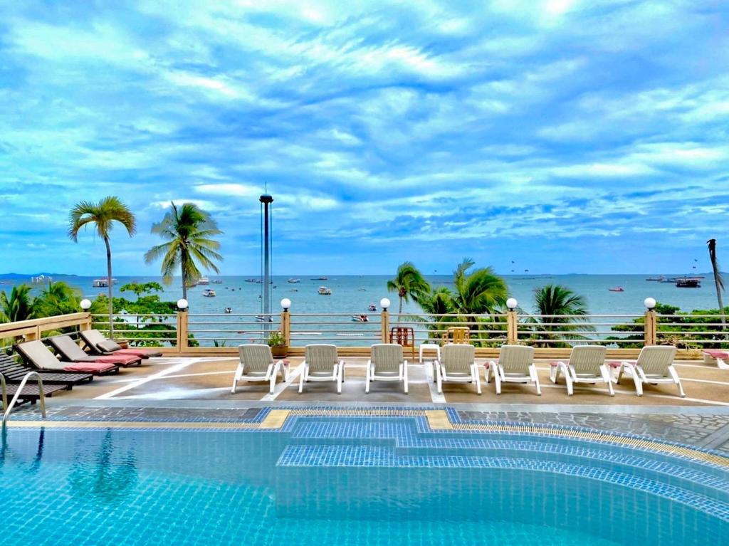 einen Pool mit Stühlen und das Meer im Hintergrund in der Unterkunft AA Hotel Pattaya in Pattaya