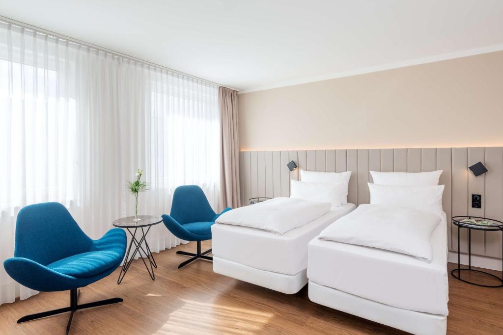 a hotel room with two beds and blue chairs at NH Köln Altstadt in Cologne