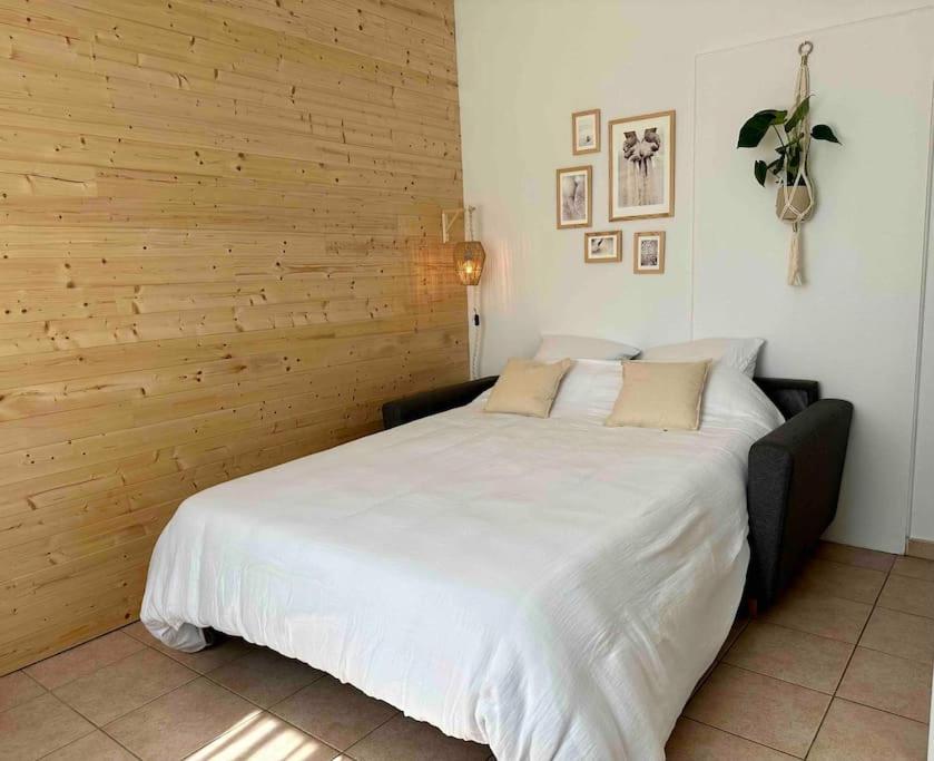 a large white bed in a room with a wooden wall at Appartement lumineux Parking Privé Gratuit in Bourg-en-Bresse