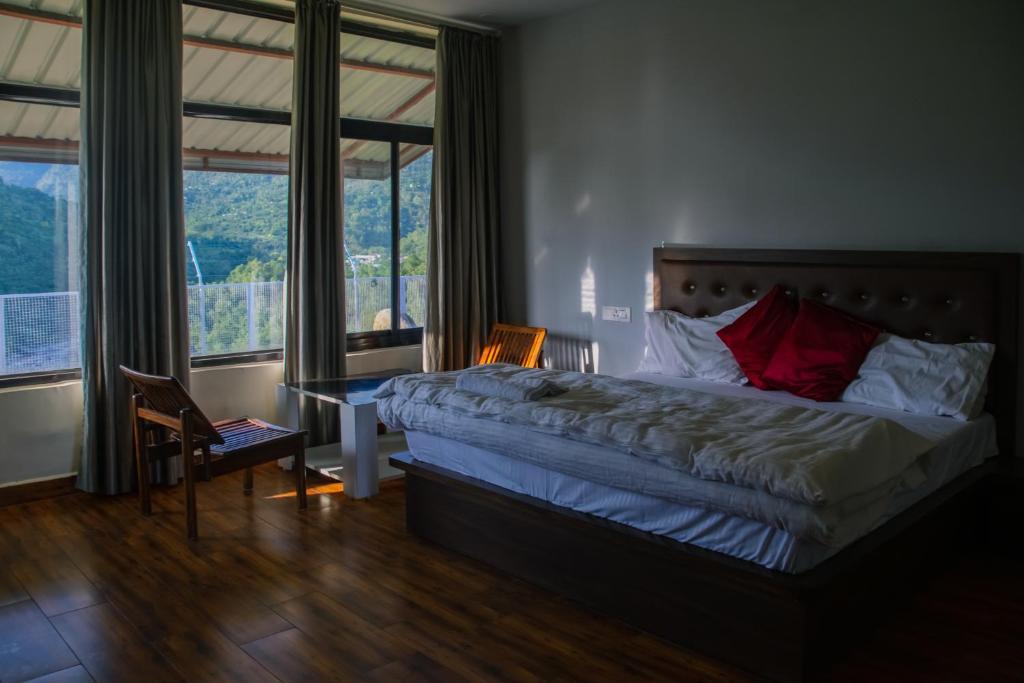 a bedroom with a bed and a desk and windows at Dhauladhar View Village Resort in Dharmsāla