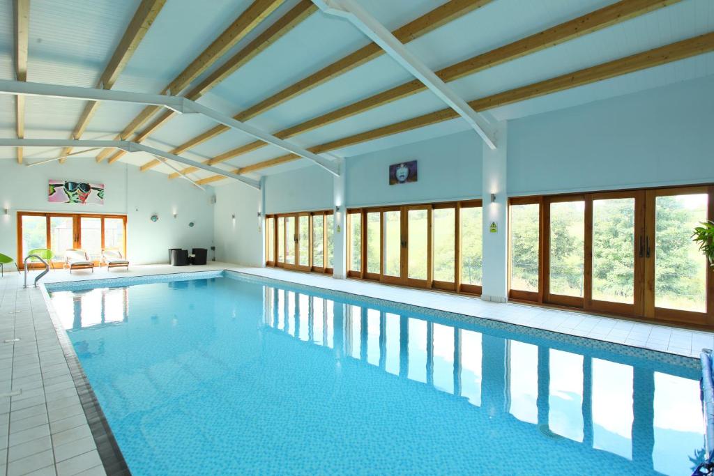 a large swimming pool with a ceiling and windows at Woodshed Cottage in Ashbourne