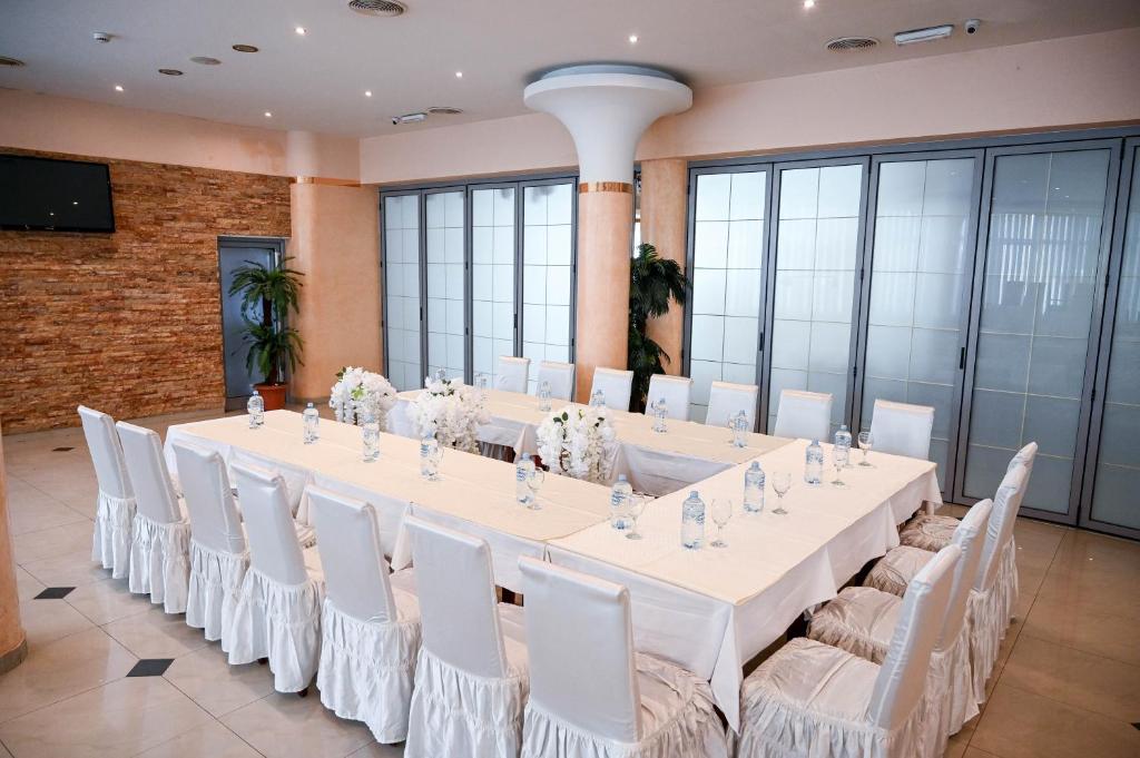 a long table with white chairs and a large room with windows at Hotel LIBERO Delchevo in Delčevo