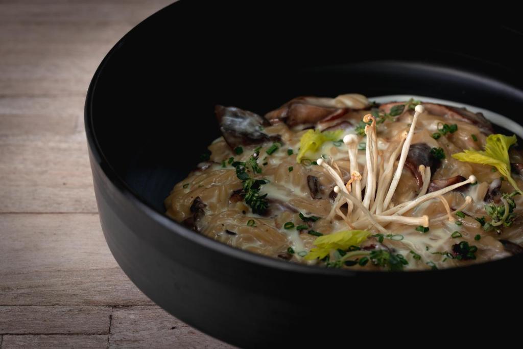 a black bowl of food with noodles and mushrooms at The Bay Hotel & Suites in Vasilikos