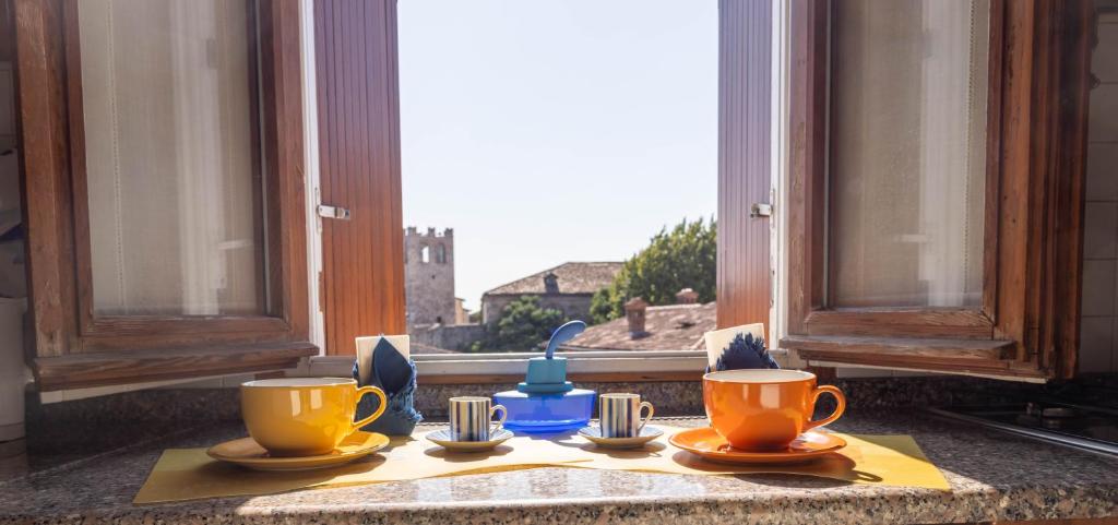 デセンツァーノ・デル・ガルダにあるLa Chicca sui Tetti Centro&Lago By Case al Lagoの窓の前にカップとソーサーが2つ置かれたテーブル