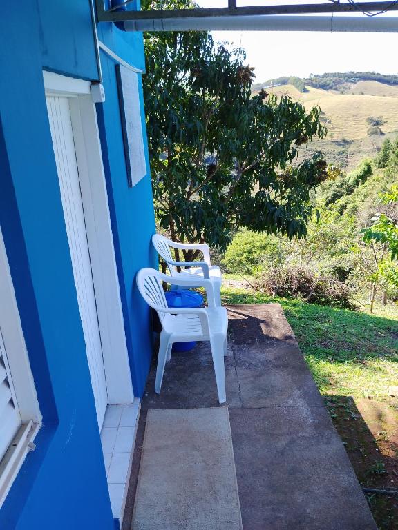 2 chaises blanches assises sur la terrasse couverte d'une maison bleue dans l'établissement Rancho Lux, à Águas de Lindóia