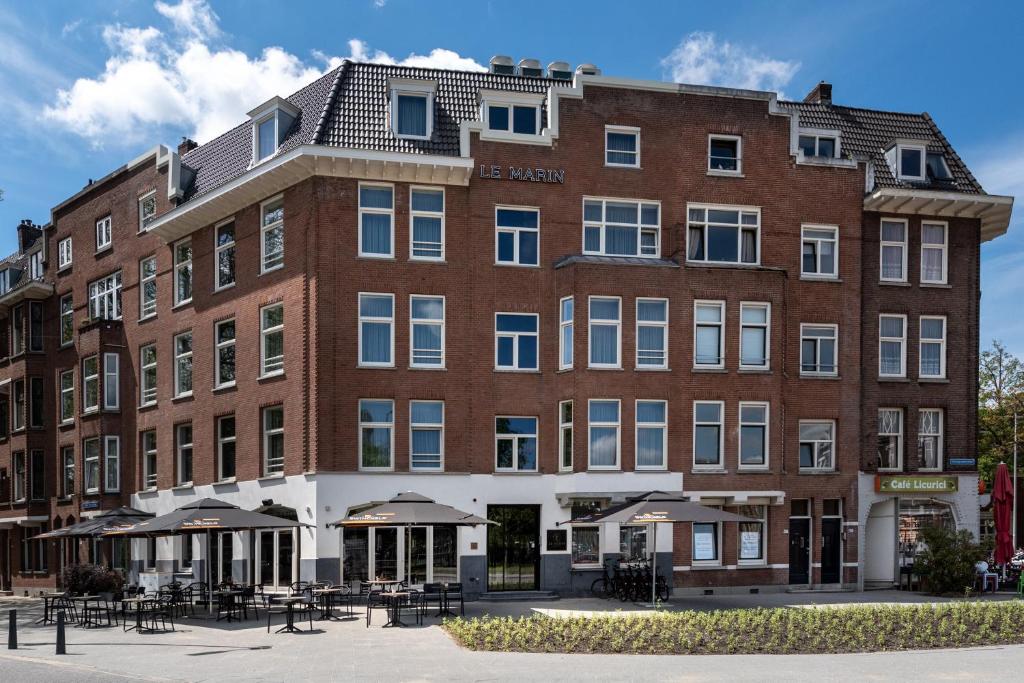 een groot gebouw van rode baksteen met tafels en parasols bij Le Marin Hotel Rotterdam City - Handwritten Collection in Rotterdam