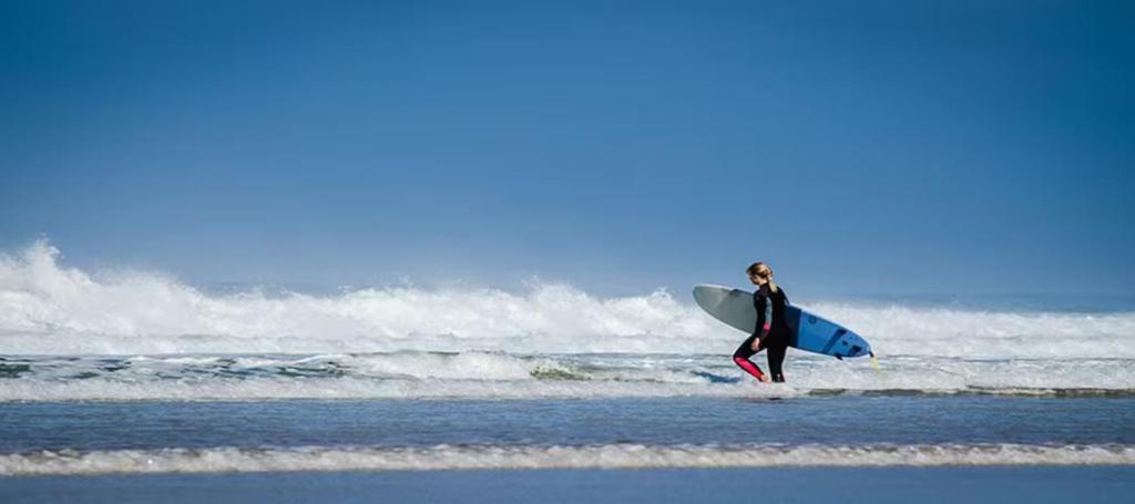 une personne se promenant dans l'océan avec une planche de surf dans l'établissement BUD HOUSE MAGNIFIQUE VILLA PROCHE DE LA MER, à Longeville-sur-Mer