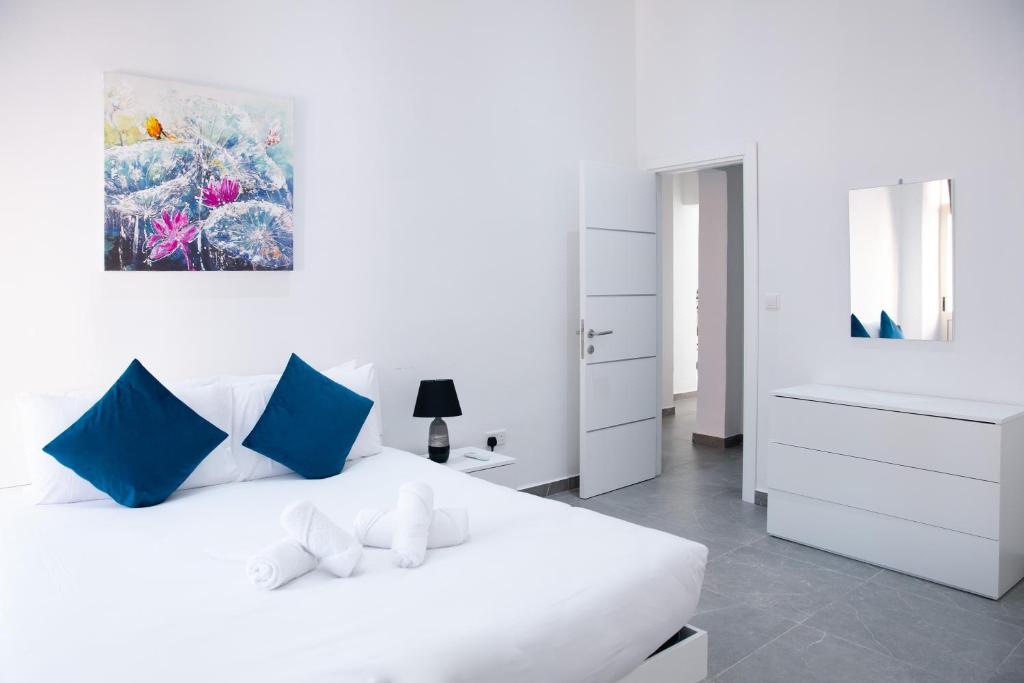 Dormitorio blanco con cama blanca y almohadas azules en Valletta Waterfront Backyard Flat, en Floriana