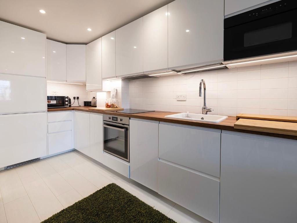 a kitchen with white cabinets and a sink at Luxury Haven with King Suites and Parking in London