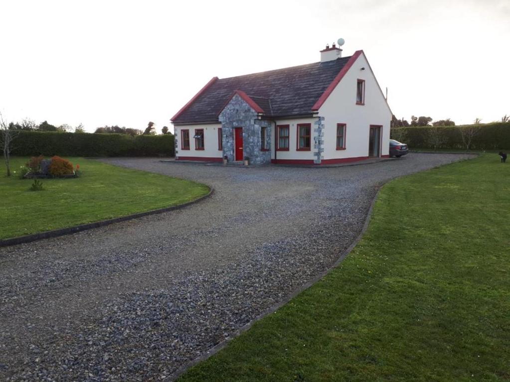 een wit huis met een rode deur op een grindweg bij Ballytigue House in Droíchead an Chláir