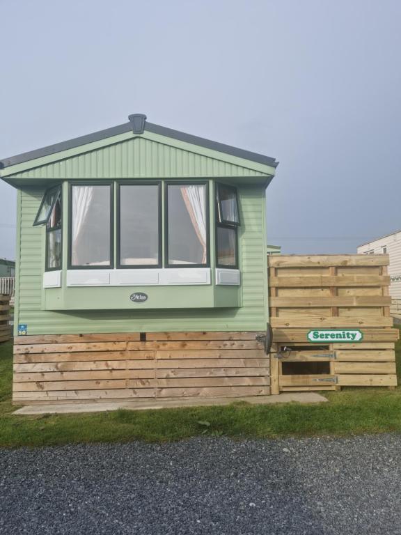 a green tiny house sitting on top of a wooden wall at Serenity in Monreith