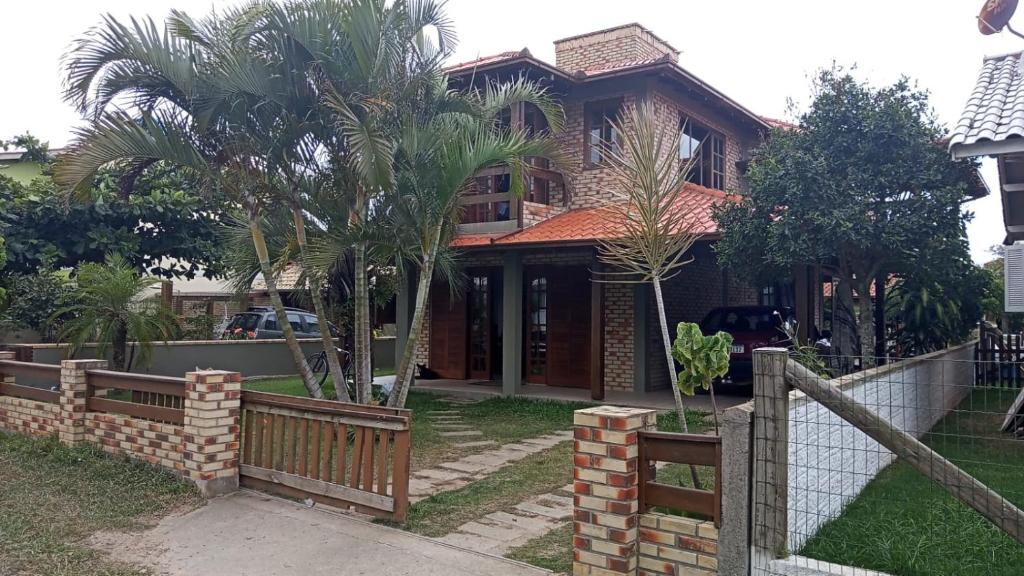 a house with a fence and palm trees in front of it at Casa da Barra da Ibiraquera in Imbituba