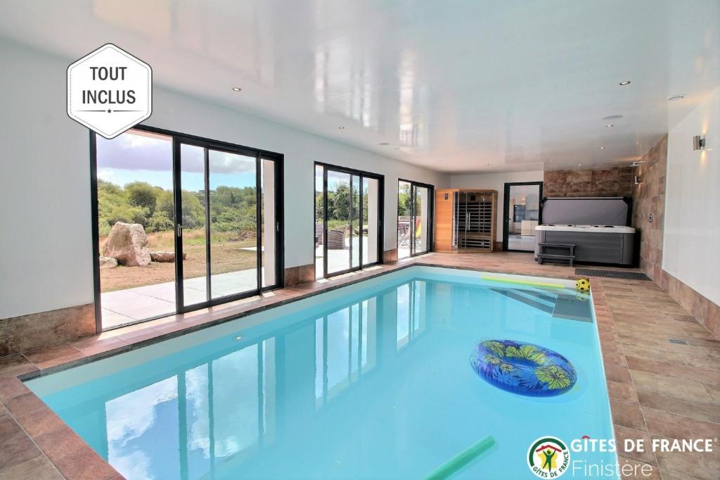 een groot zwembad in een huis met ramen bij Longère avec piscine intérieure, spa, sauna in Douarnenez
