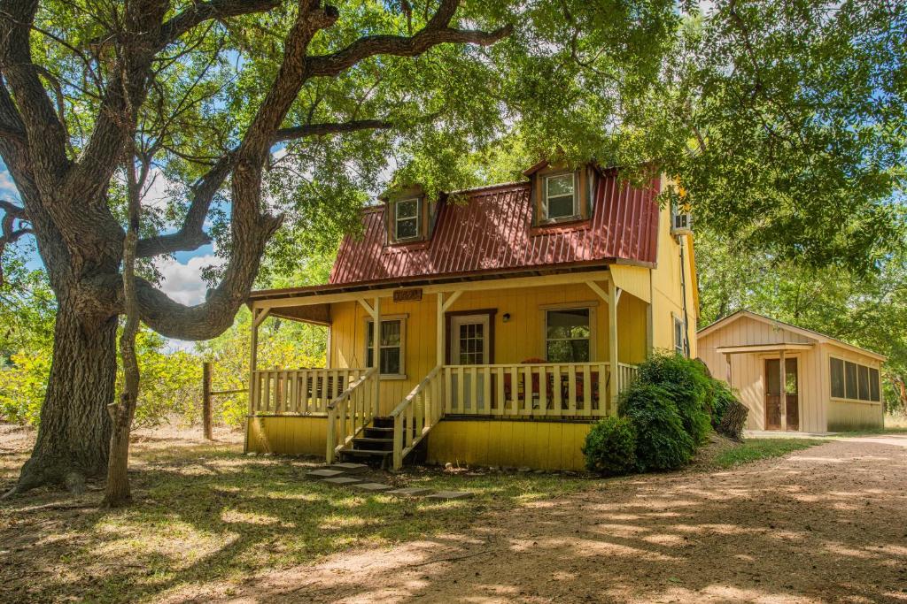 a yellow house with a red roof and a tree at Olive Cabin in Fredericksburg
