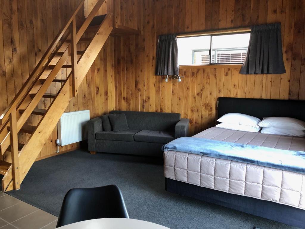 1 dormitorio con cama, sofá y escaleras en Alpine Motel, en Ohakune