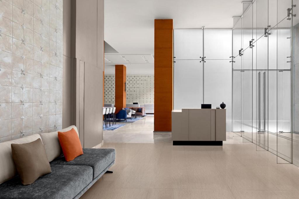 A modern lobby lounge with a grey sofa facing a reception desk and glass-walled areas.