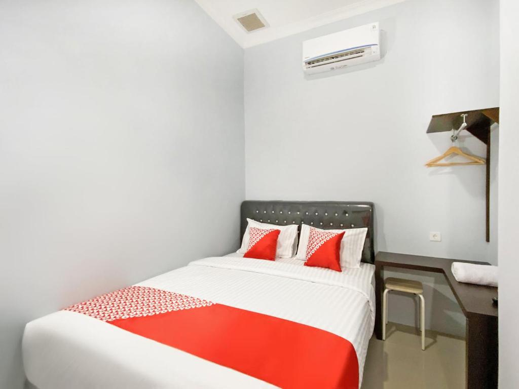a bedroom with a bed with red pillows and a desk at OYO 3160 Guesthouse Pagi Sore Syariah in Padang