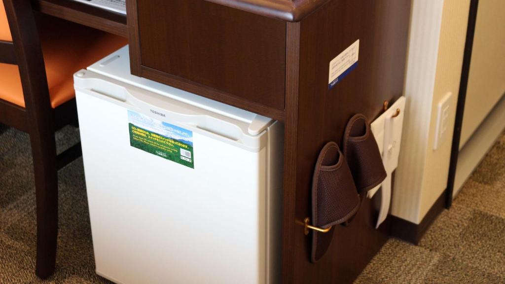 a small white refrigerator next to a wooden cabinet at Toyoko Inn Osaka Itami Airport in Toyonaka