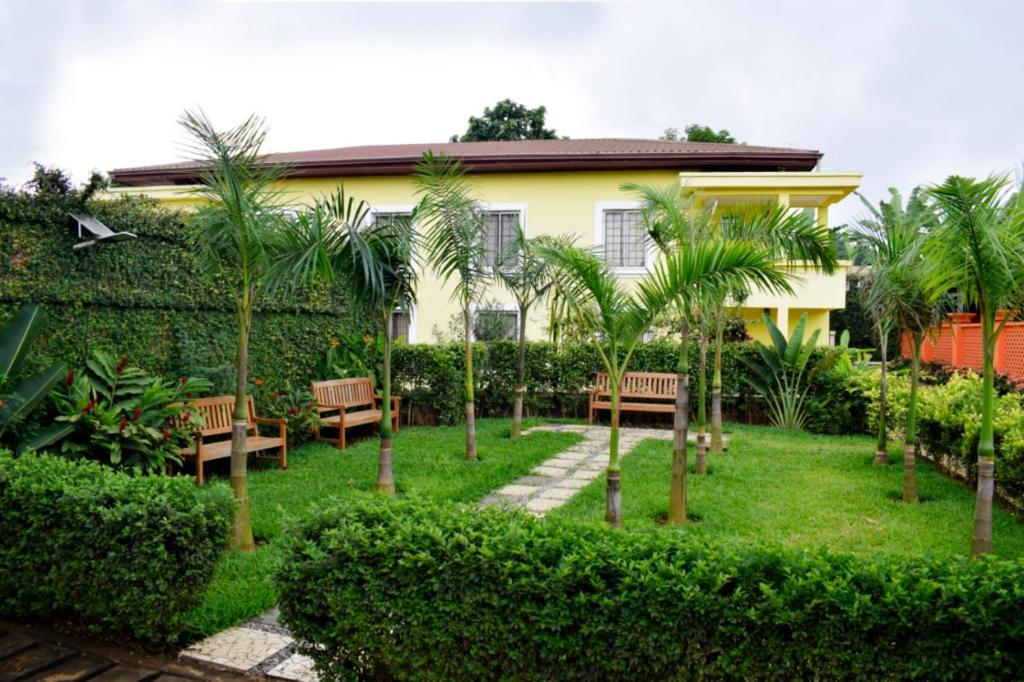 a garden with benches and palm trees in front of a house at Riad Prince Louis in Yaoundé