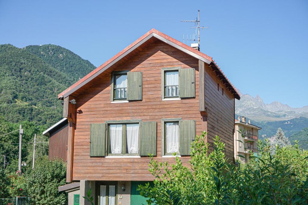 a wooden house with green windows and mountains in the background at Woodhouse paesana in Paesana