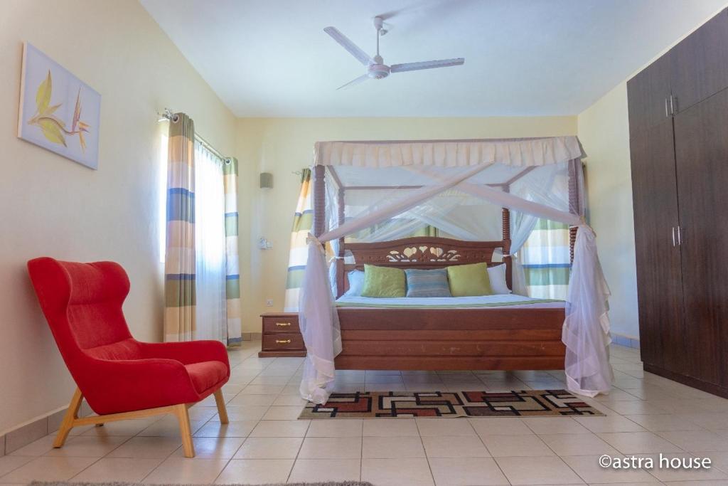 1 dormitorio con cama con dosel y silla roja en HomeAway_Luxurious Malindi en Malindi