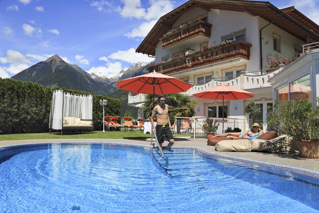 un homme debout dans une piscine avec un parasol dans l'établissement Adults only Hotel Grafenstein, à Schenna