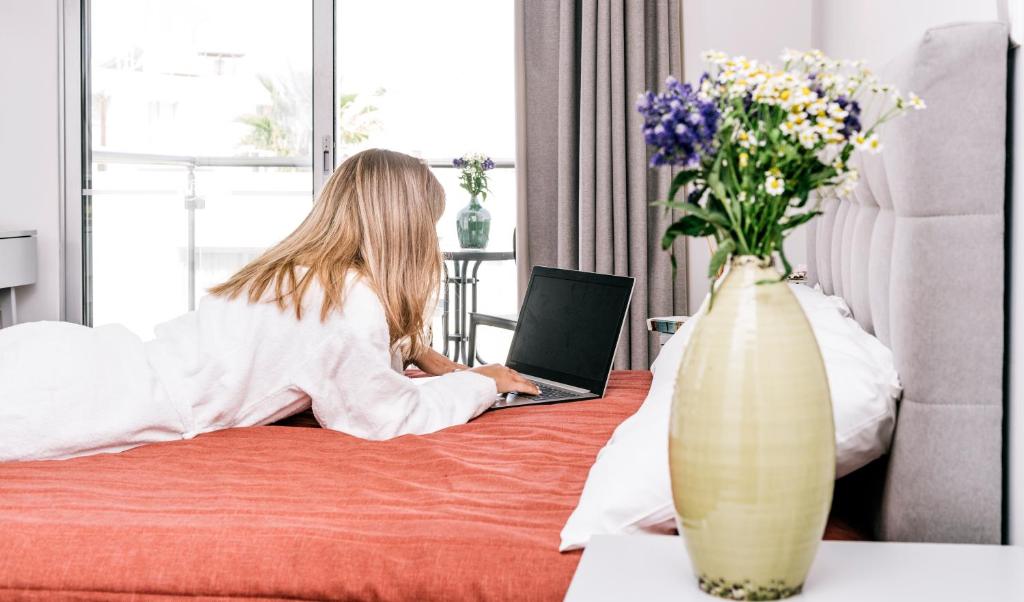 a woman laying on a bed with a laptop at River View Boutique Apts in Ayia Napa
