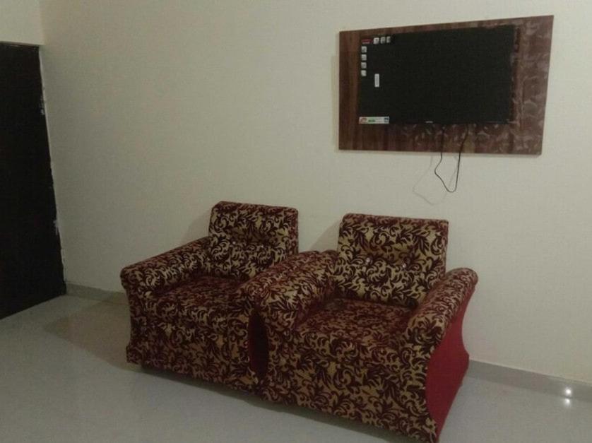 OYO Raj Villas في Satna: غرفة معيشة مع كرسي وتلفزيون بشاشة مسطحة