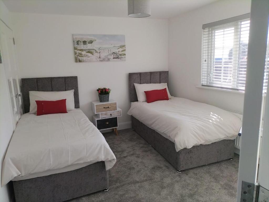 Duas camas num quarto com almofadas brancas e vermelhas em Binevenagh View, Magilligan Holiday Let em Limavady